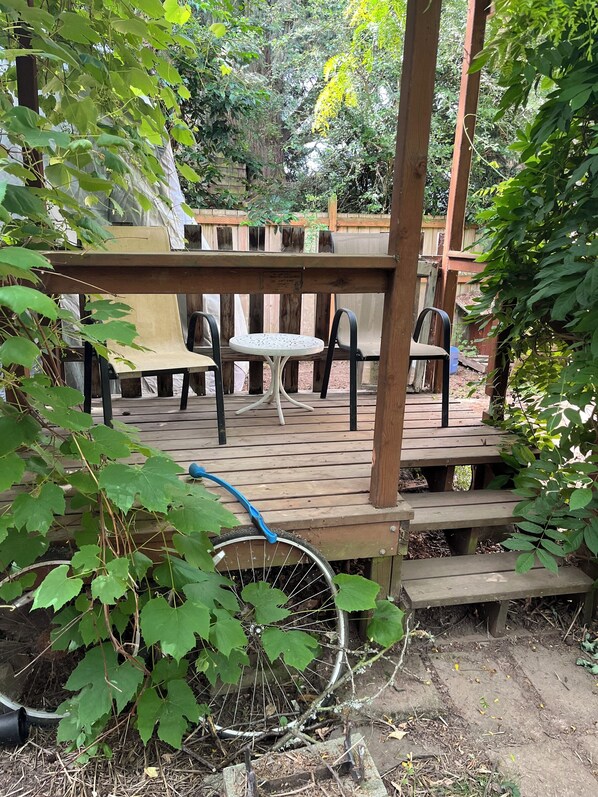 A wooden deck with a table and chairs, surrounded by greenery.
