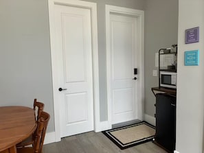 A room with two white doors, a wooden dining table, a black cabinet, and a doormat.
