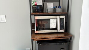 A compact kitchenette with a microwave, a small refrigerator, and a blue shoe rack.