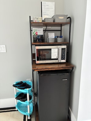 A compact kitchenette with a microwave, a small refrigerator, and a blue shoe rack.