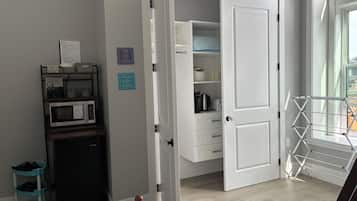 A room with a white door, a microwave, a shelf with storage bins, a chair, and a window with a view.