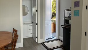 A room with a dining table, chairs, a white cabinet, a black trash bin, and a door leading to an outdoor area with a wooden deck.
