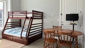A room with a bunk bed, a table with chairs, and a television on a stand.