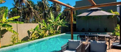 A poolside area with lounge chairs, a wooden pergola, and a view of palm trees.