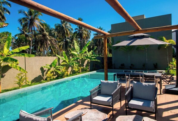 A poolside area with lounge chairs, a wooden pergola, and a view of palm trees.