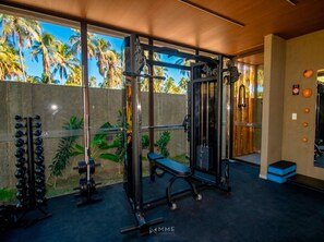 A gym with weightlifting equipment, a bench, and a wall with palm trees. - Cond Azuk Patacho: Leisure and Beach by MME (Porto de Pedras)