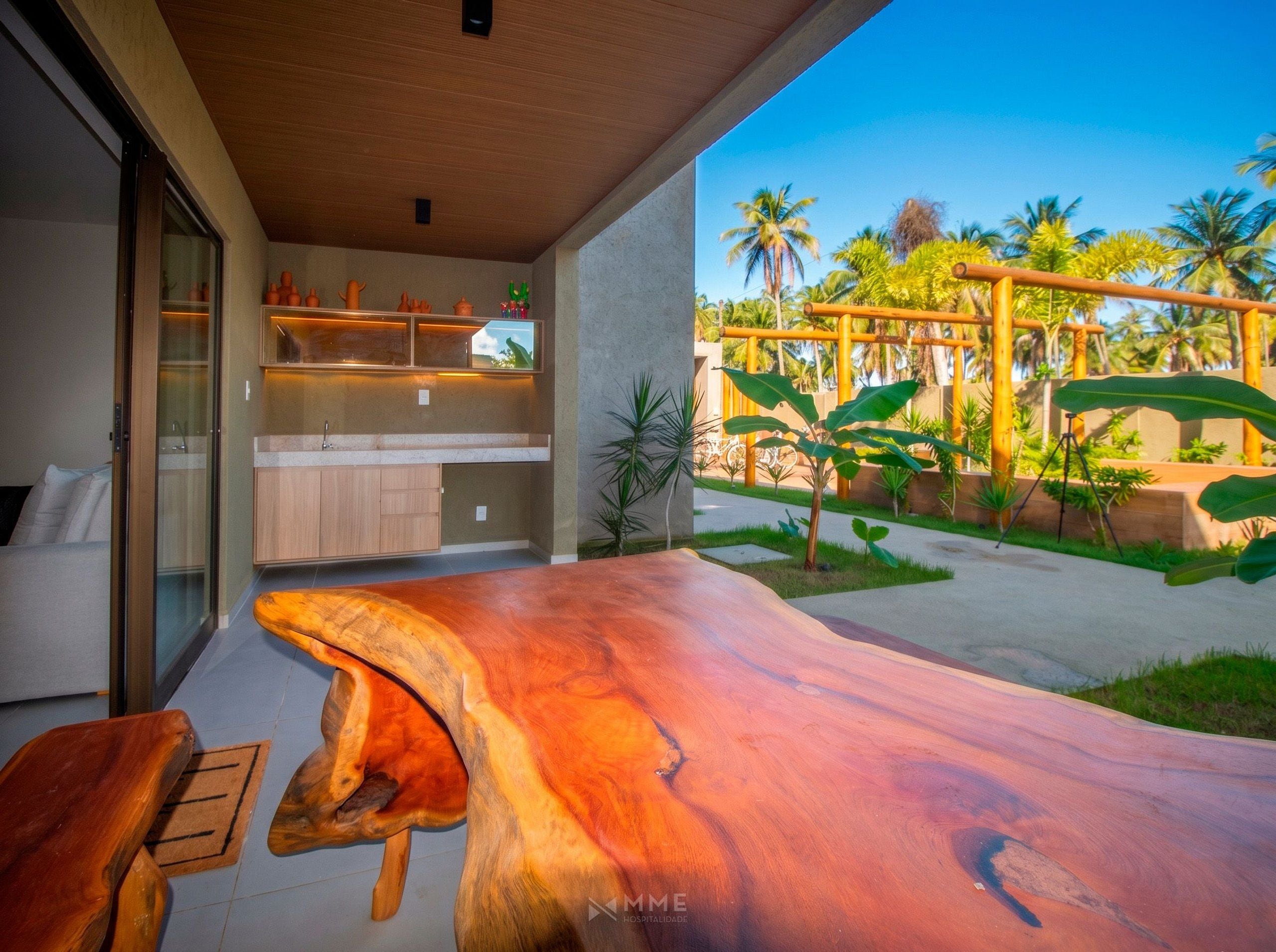 Uma cozinha moderna com uma ilha grande, uma porta de vidro que dá para uma varanda, e vista para um jardim tropical.