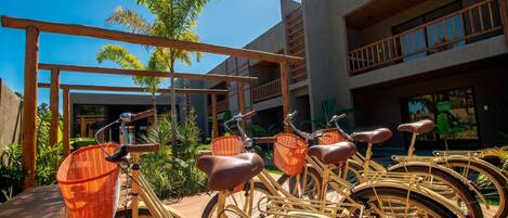 Une rangée de vélos équipés de paniers, une pergola en bois et un bâtiment doté de balcons.