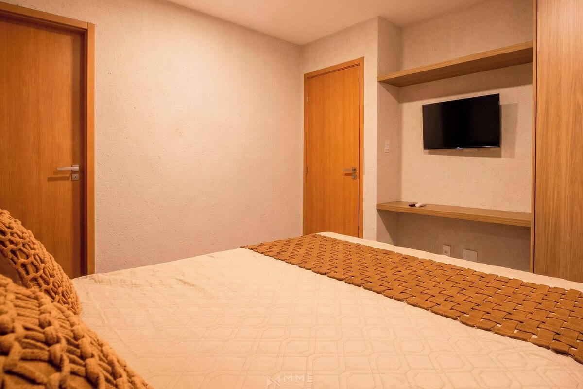 A bedroom with a bed, a television mounted on the wall, and wooden doors.