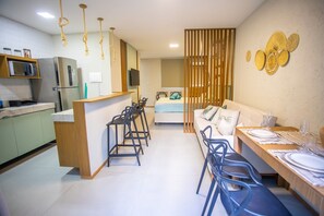A modern kitchen with a bar area, a dining space with chairs and a table set for two, and a living area with a sofa and a bed.