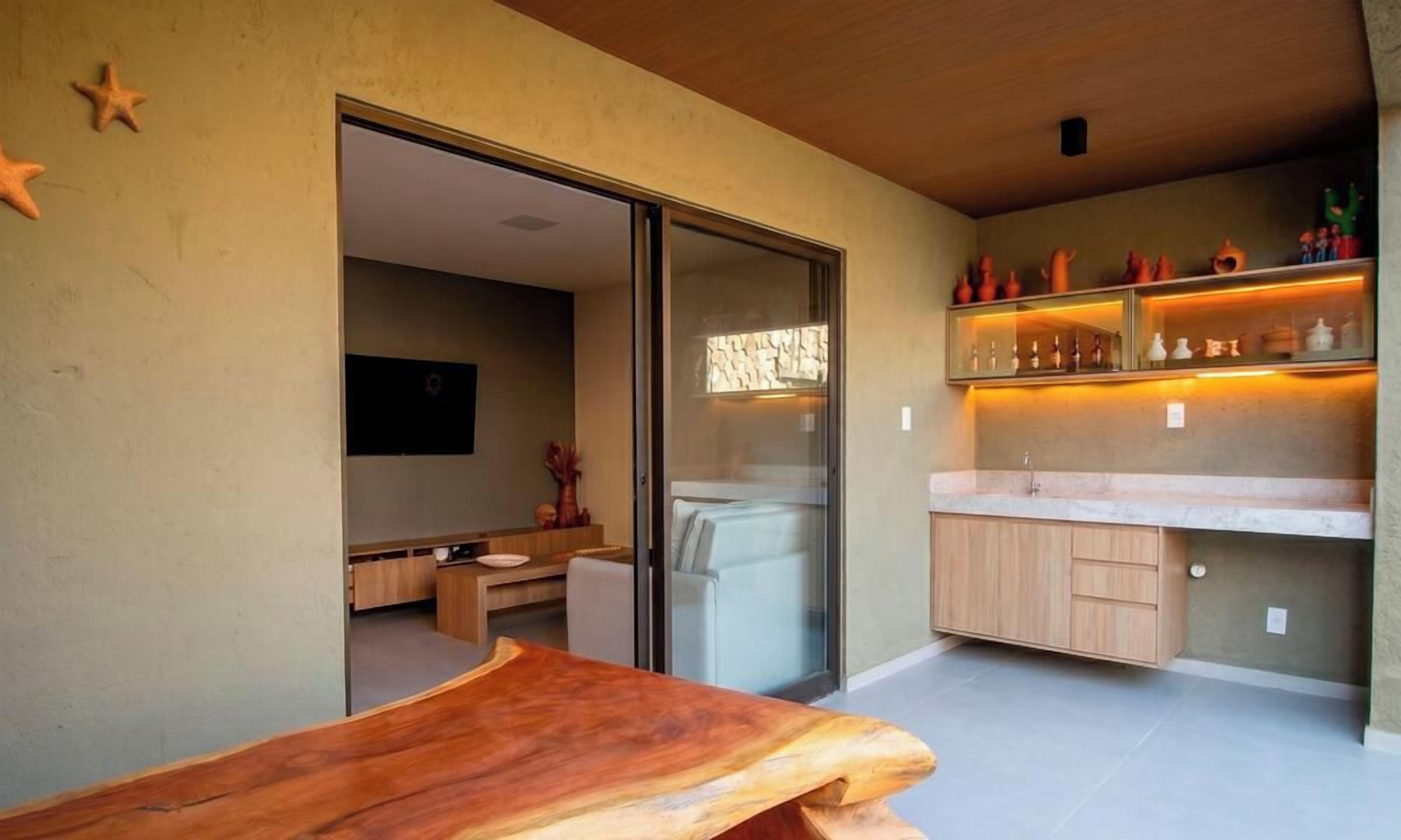 Uma cozinha moderna com bancada de madeira, porta de vidro que dá para uma sala de jantar e prateleira com objetos decorativos.