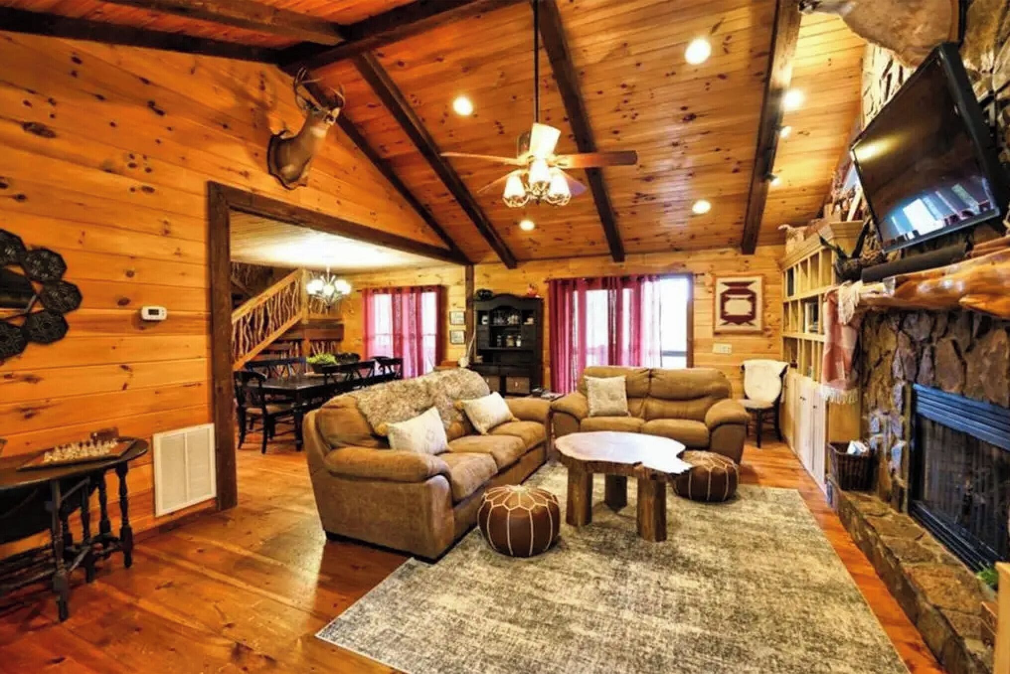 A cozy log cabin interior with a fireplace, a television, and a dining area.