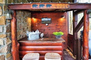 Ein Barbereich aus Holz mit einem Schild mit der Aufschrift 'Lodge', einem darüber montierten Fernseher und einem Eimer mit Flaschen und Gläsern.