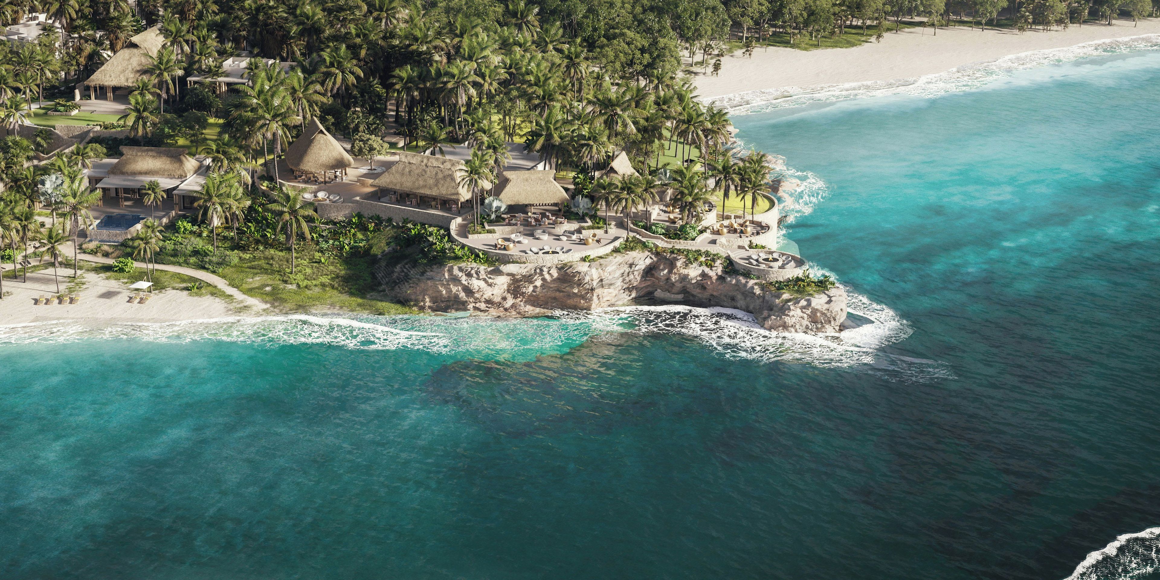 An aerial view of a coastal resort with multiple thatched-roof structures, a sandy beach, and clear turquoise waters.