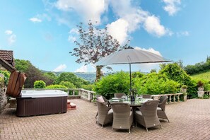 Eine Terrasse im Freien mit Whirlpool, Esstisch und Stühlen, umgeben von üppiger Bepflanzung und schöner Aussicht.