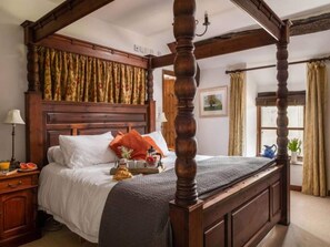 Ein Himmelbett mit Holzkopfstütze, ein Nachttisch mit Lampe und ein Fenster mit Vorhängen.
