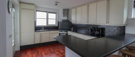 Cozinha com bancada preta, armários brancos, uma janela e piso de madeira.
