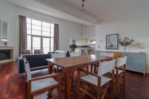 A spacious living area with a wooden dining table and chairs, a kitchen in the background, and a large window with curtains. - Beachfront Villa With Terrace & Views (Makkum)