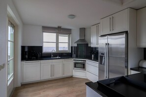 A modern kitchen with white cabinetry, a stainless steel refrigerator, a built-in oven, and a window with a view. - Beachfront Villa With Terrace & Views (Makkum)