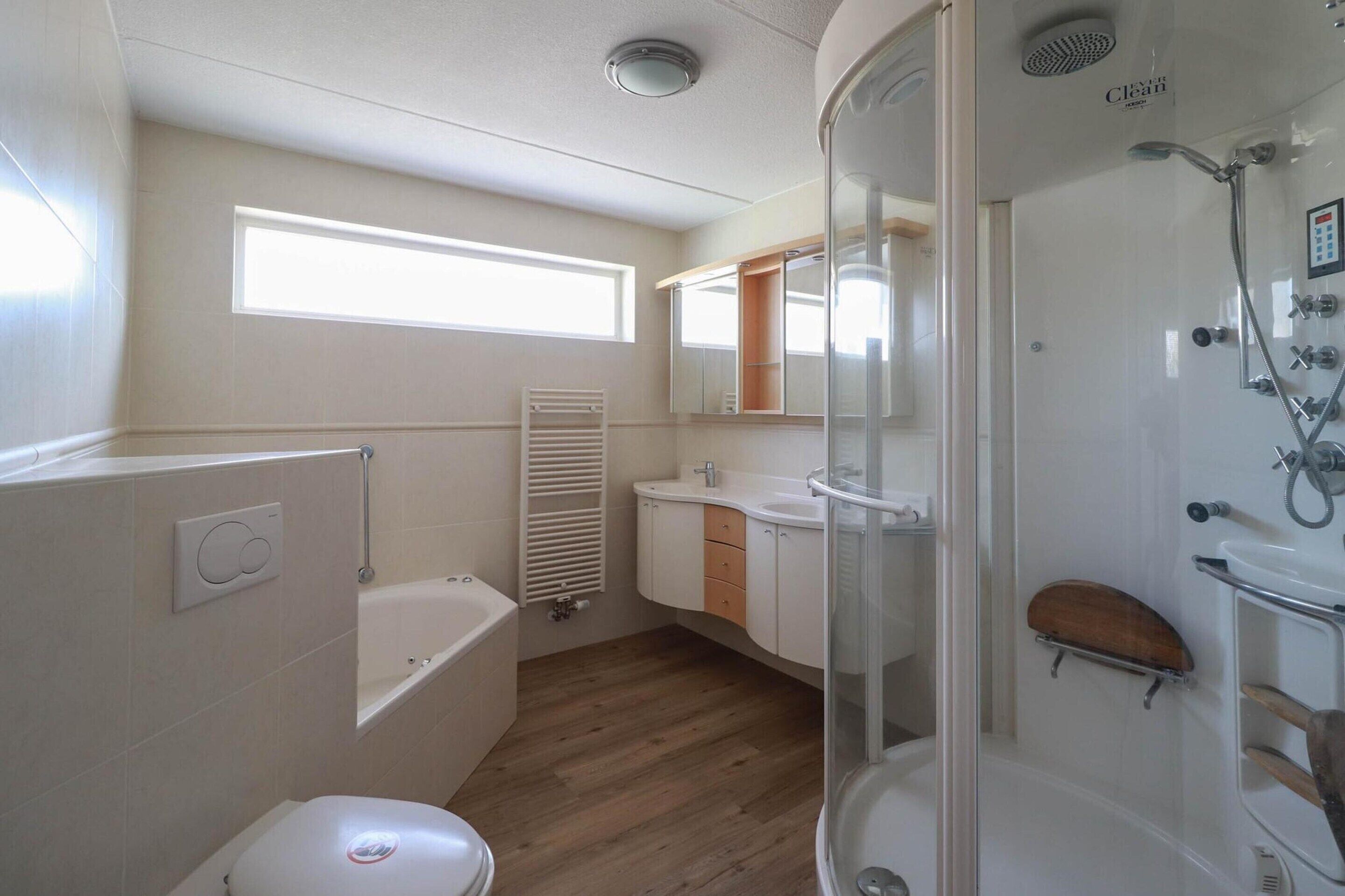 Ein kleines Badezimmer mit Badewanne, Toilette, Dusche und einem Fenster für natürliches Licht.