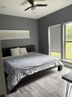 A bedroom with a bed, a ceiling fan, a window, and a painting on the wall. - Charming 3-bedroom house in soothing Coldspring with outdoor kitchen and firepit (Coldspring)