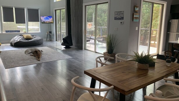 Ein stilvolles Wohnzimmer mit Esstisch aus Holz, weißen Stühlen, einem grauen Sitzsack und einem Hund.