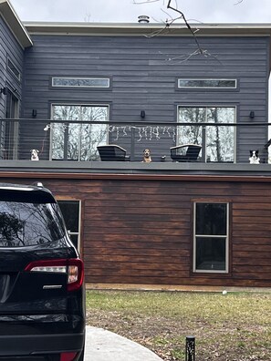 A modern two-story house with a balcony, a car parked in front, and a dog on the balcony. - Charming 3-bedroom house in soothing Coldspring with outdoor kitchen and firepit (Coldspring)