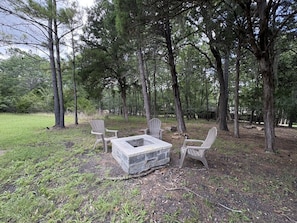 An outdoor seating area with stone fire pit and Adirondack chairs in a wooded setting. - Charming 3-bedroom house in soothing Coldspring with outdoor kitchen and firepit (Coldspring)