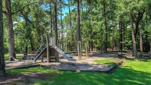 Ein Spielplatz mit Rutsche und Klettergerüst, umgeben von Bäumen.