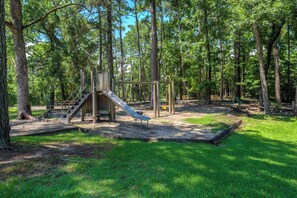 Ein Spielplatz mit Rutsche und Klettergerüst, umgeben von Bäumen.