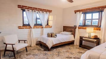 Ein Schlafzimmer mit Bett, Stuhl, Nachttisch und einem Fenster mit Vorhängen.