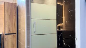 A modern bathroom with a glass-enclosed shower, a wooden cabinet, and a marble wall.