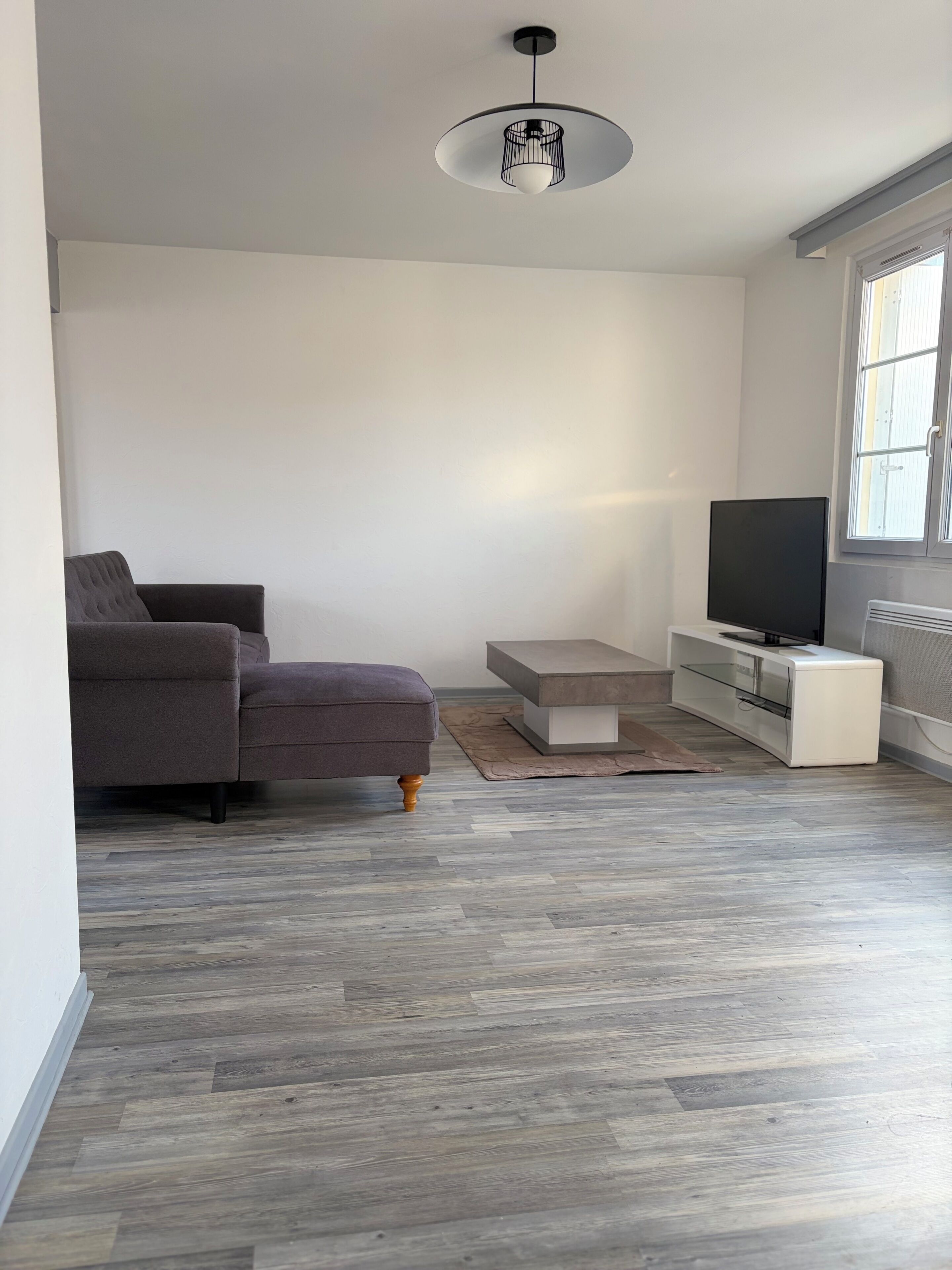 A modern living room with a grey sofa, a television, and a wooden floor.