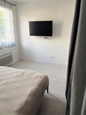 Une chambre à coucher avec un lit, un téléviseur à écran plat fixé au mur et une fenêtre ornée de rideaux légers.