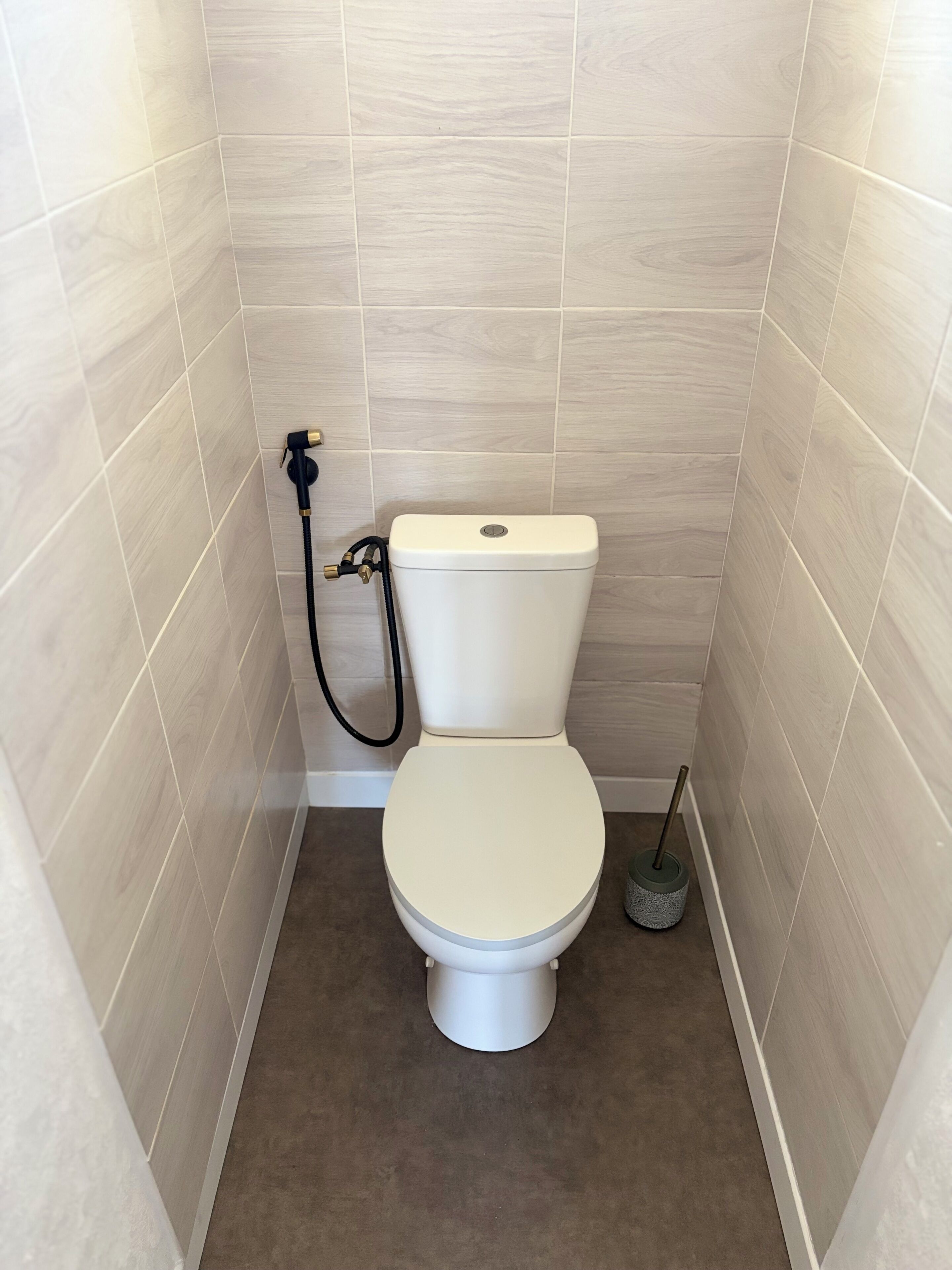 A small, modern bathroom with a toilet, a shower hose, and a floor scrubber.