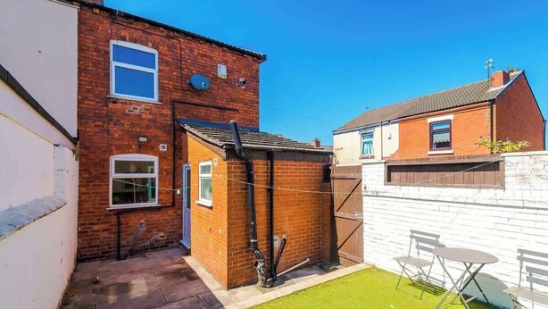 A residential property with a brick house, a small fenced yard, and a white wall. - Stylish 2 Bedroom Home Sleeps 4 (St Helens)