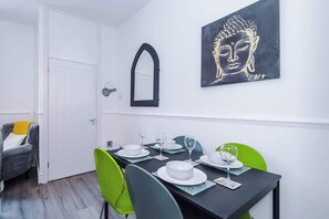 A dining area with a table set for four, a mirror, and a Buddha painting on the wall. - Stylish 2 Bedroom Home Sleeps 4 (St Helens)