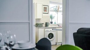 A room with a dining table set for four, a washing machine, and a window with a plant. - Stylish 2 Bedroom Home Sleeps 4 (St Helens)