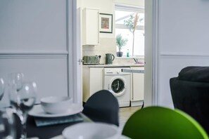 Ein Zimmer mit Esstisch für vier Personen, einer Waschmaschine und einem Fenster mit Pflanze.
