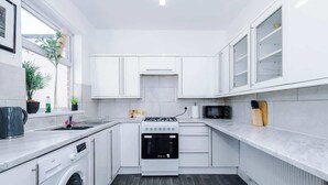 A compact kitchen with white cabinets, a built-in oven, a microwave, and a washing machine. - Stylish 2 Bedroom Home Sleeps 4 (St Helens)