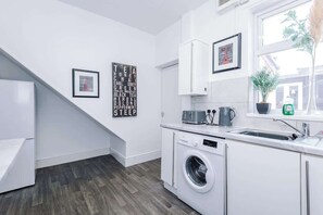 A modern kitchen with a built-in washing machine, white cabinetry, and a window with a view. - Stylish 2 Bedroom Home Sleeps 4 (St Helens)