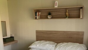 Una cama bien hecha con cabecera, un estante pequeño encima y una toalla verde sobre la cama.