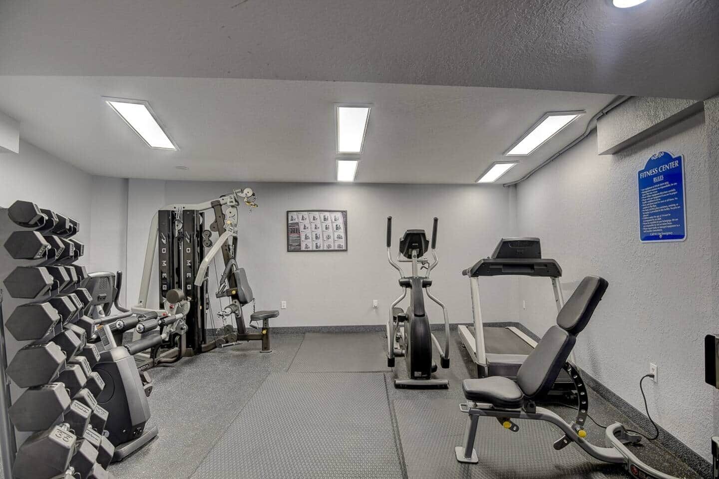 A gym with various exercise equipment including dumbbells, a weight machine, and cardio machines.