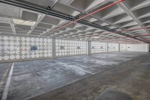 Eine große, leere Tiefgarage mit Betonböden und -wänden, die ein gitterförmiges Muster aus weißen Feldern sowie rote und blaue Rohre an der Decke zeigt.