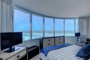 Een hotelkamer met een groot erkerraam, een bed, een televisie en een bureau.