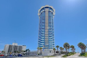 Ein hohes, zylindrisches Hotel mit blauer und weißer Fassade, in der Nähe einer von Palmen gesäumten Straße.