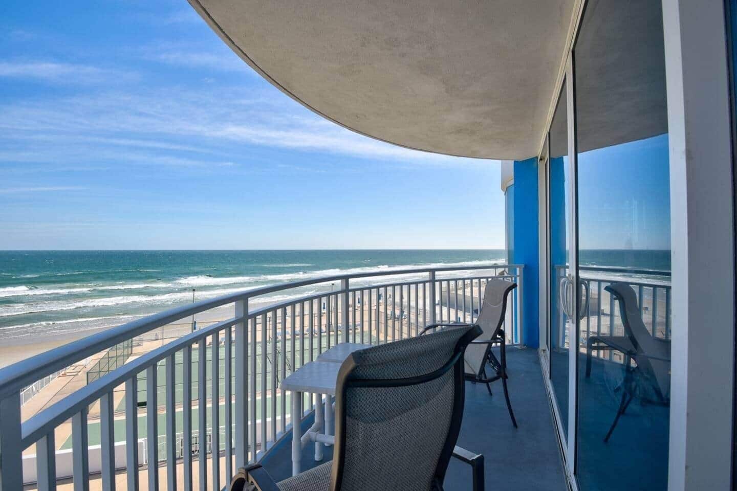 Un balcón con vista a la playa y al océano, una mesa y dos sillas.