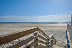 Een houten promenade langs het strand, leidend naar de oceaan, met een heldere lucht.