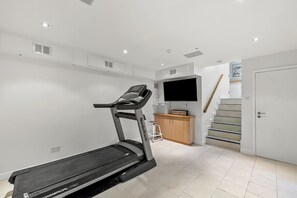 Ein Heimfitnessraum mit Laufband, Fernseher und Treppe.