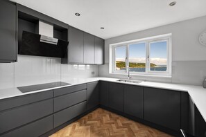 Eine moderne Küche mit dunklen Schränken, einer weißen Arbeitsplatte und einem Fenster mit Meerblick.